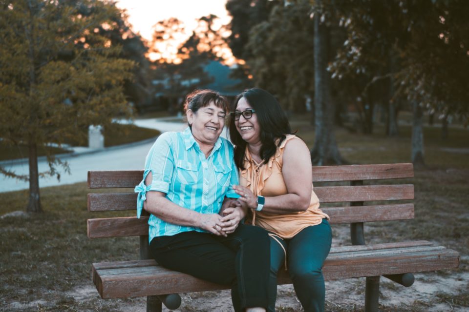 two women sit on park bench as sun sets