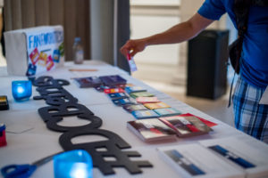 arm reaching out to registration table with stickers in various colors, #DCBeings signs, and a pair of blue scissors