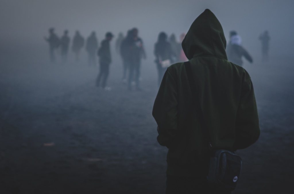 child in dark green hoodie looks toward crowd through thick fog