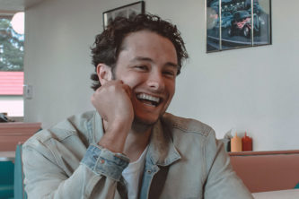 Man sitting at booth in restaurant leaning on one hand and laughing