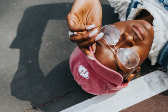 young woman with red hat and large glasses laying on pavement.